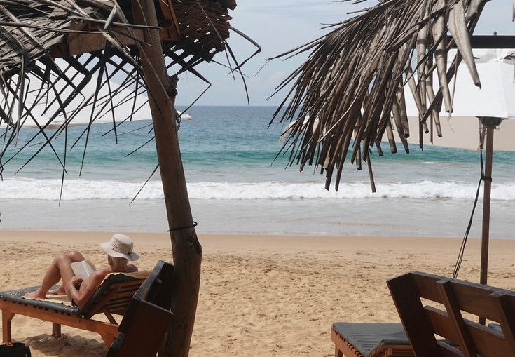a woman sits under an umbrella on the beach