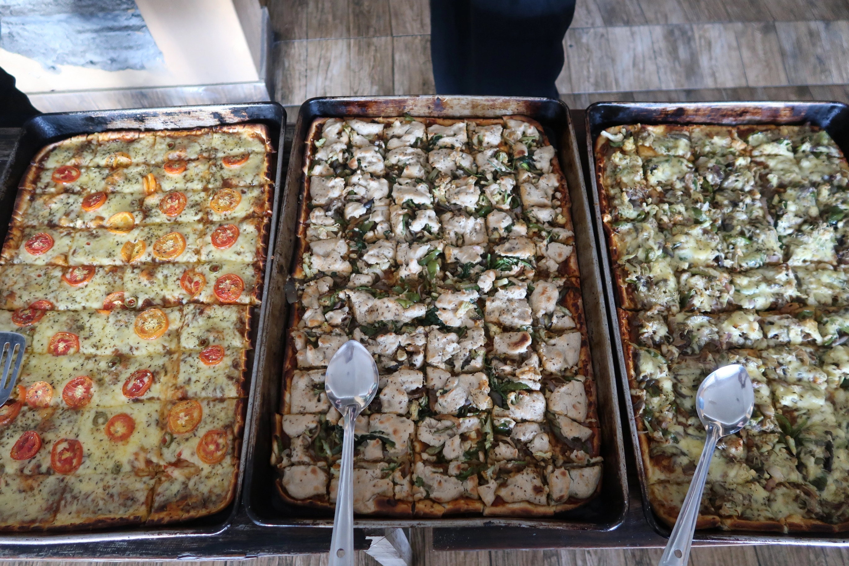 three trays of pizza with spoons on a table .