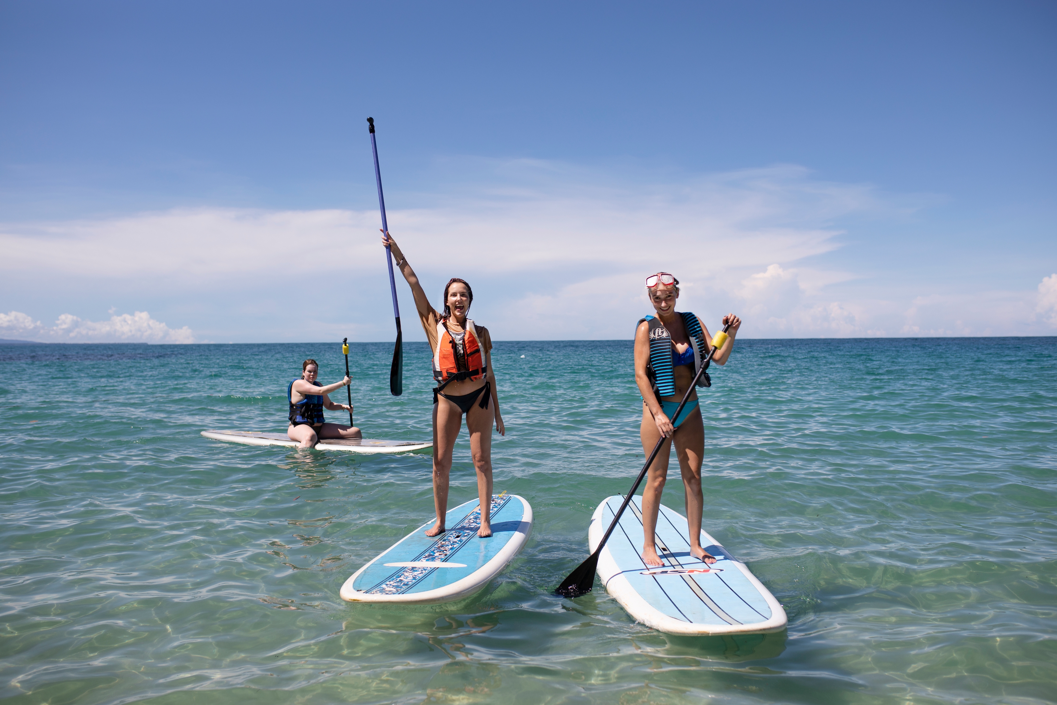 två kvinnor står på paddle boards i havet.