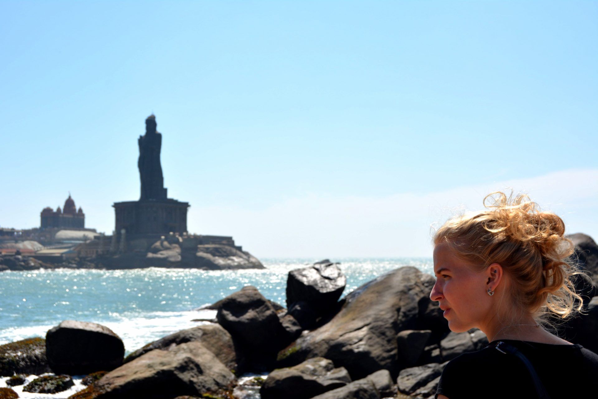 a woman is standing on a rocky beach with a statue in the background .