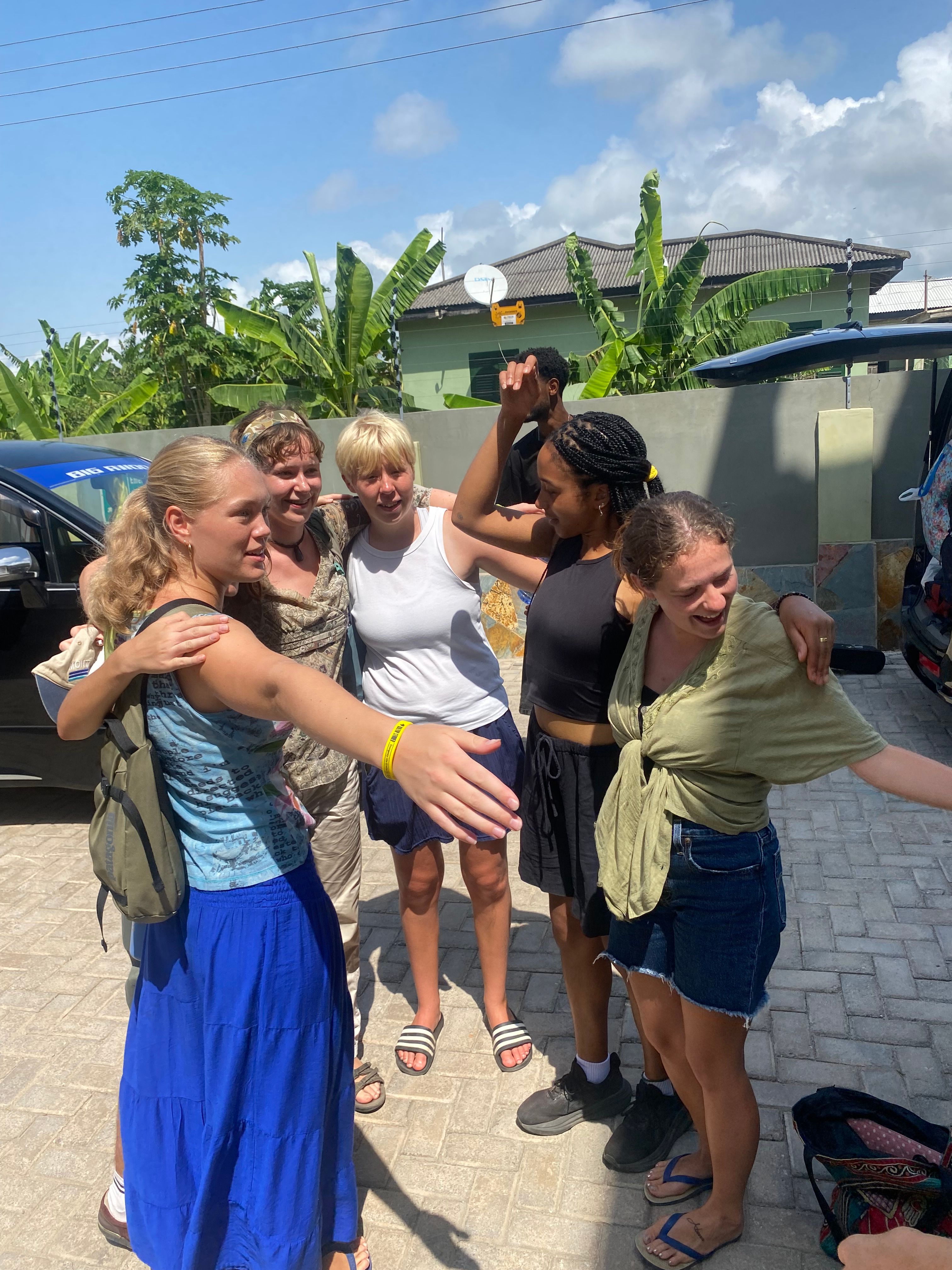 A joyful group of women pose outdoors in a tropical setting.