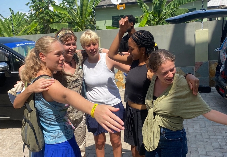 A joyful group of women pose outdoors in a tropical setting.