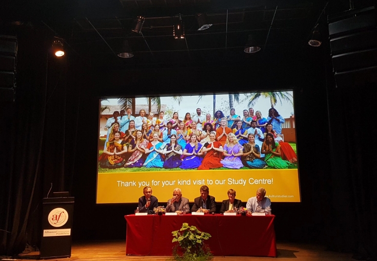 a group of people are sitting at a table in front of a large screen .