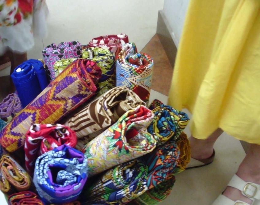 a woman in a yellow dress is standing next to a pile of colorful fabrics