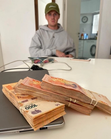 a man sits at a table with stacks of money on top of a laptop