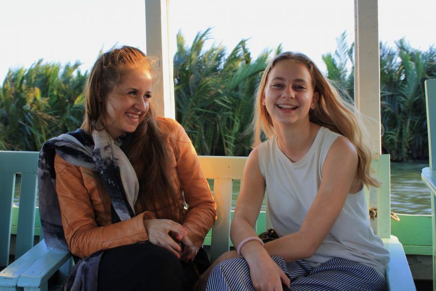 two young women are sitting on a bench in front of a body of water .