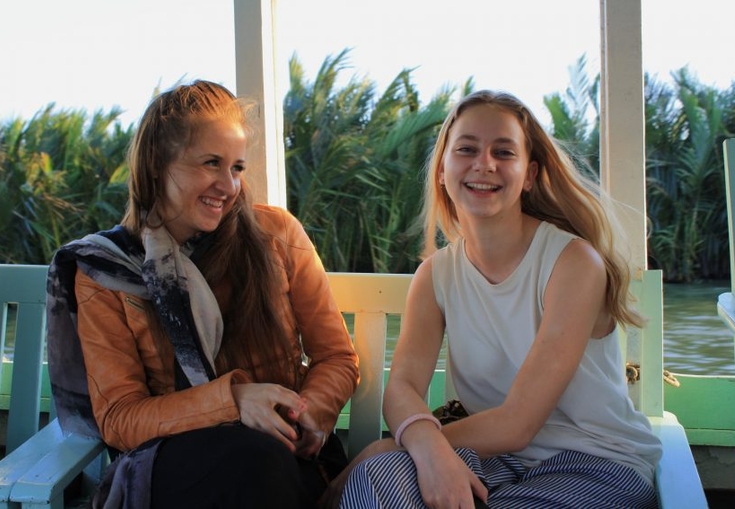 two young women are sitting on a bench in front of a body of water .