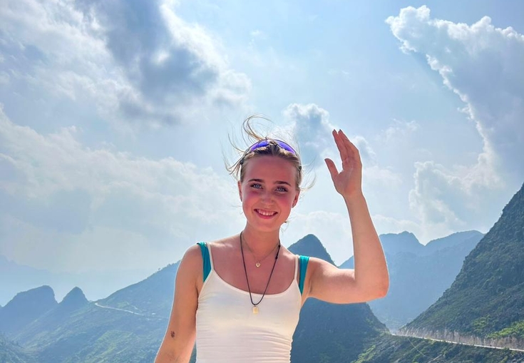 a woman in a white tank top and blue shorts is standing on top of a mountain .