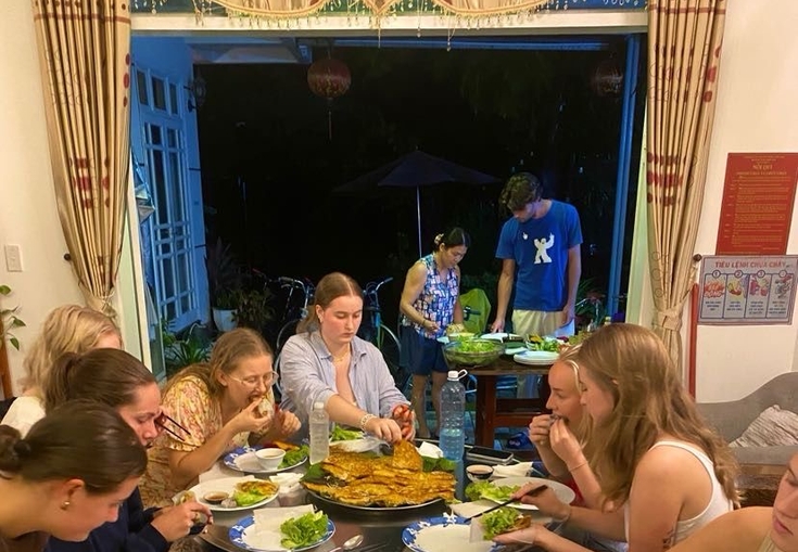 a group of people are sitting around a table eating food and drinking fanta