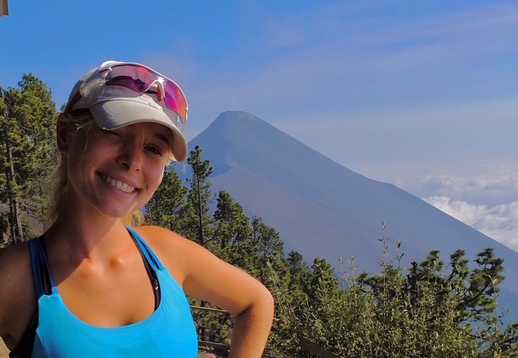 en kvinne som har på seg solbriller og en hatt, står foran et fjell.