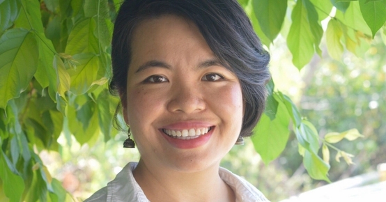 a woman in a white shirt is smiling in front of a tree .