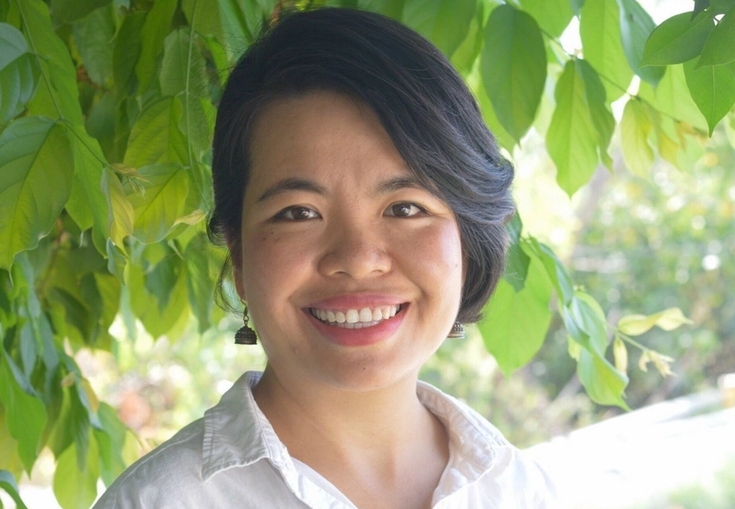 a woman in a white shirt is smiling in front of a tree .