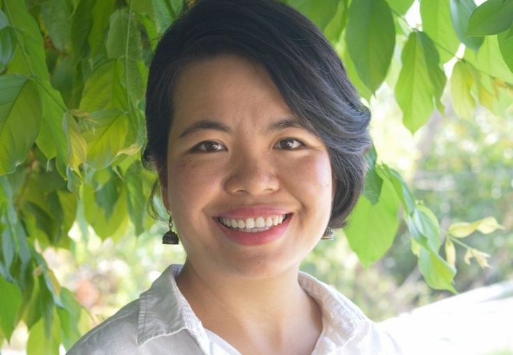 en kvinna i en vit skjorta ler framför ett träd