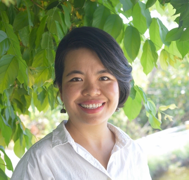 a woman in a white shirt is smiling in front of a tree .