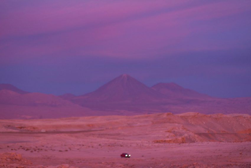a car is parked in the desert with mountains in the background at sunset .