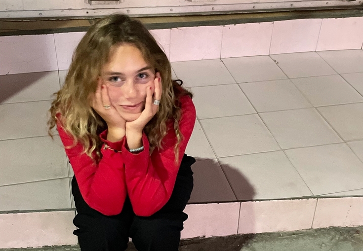 a woman in a red shirt and black pants is sitting on a tiled floor