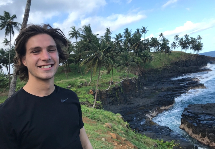 en ung man står på en klippa med utsikt över havet.