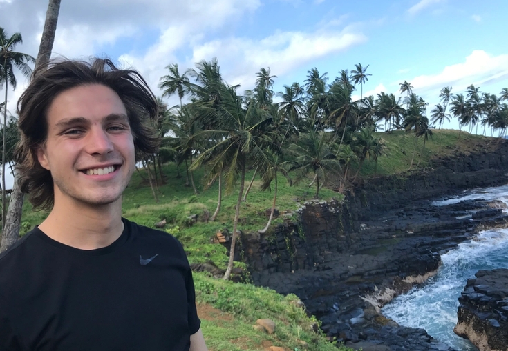 a young man is standing on a cliff overlooking the ocean.