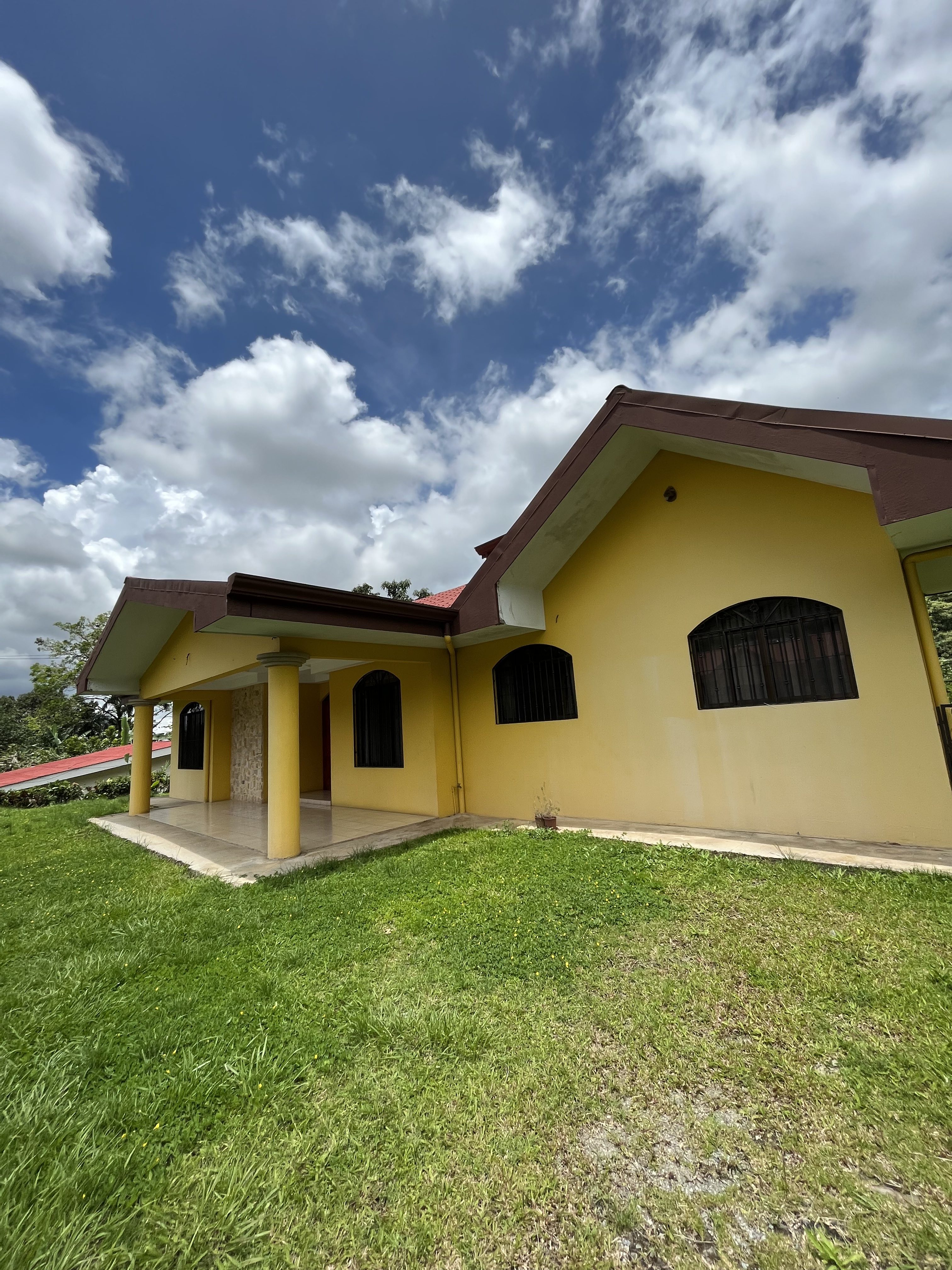 a yellow house with a brown roof is sitting on top of a lush green field .