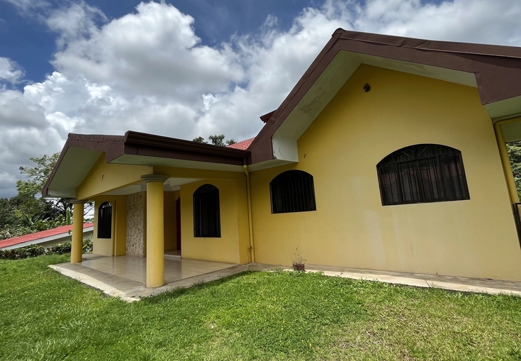 a yellow house with a brown roof is sitting on top of a lush green field .