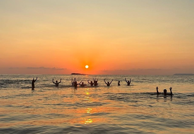 a group of people are swimming in the ocean at sunset .
