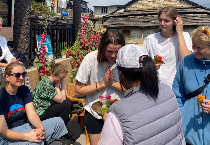 en gruppe unge kvinner sitter rundt et bord foran en bygning.