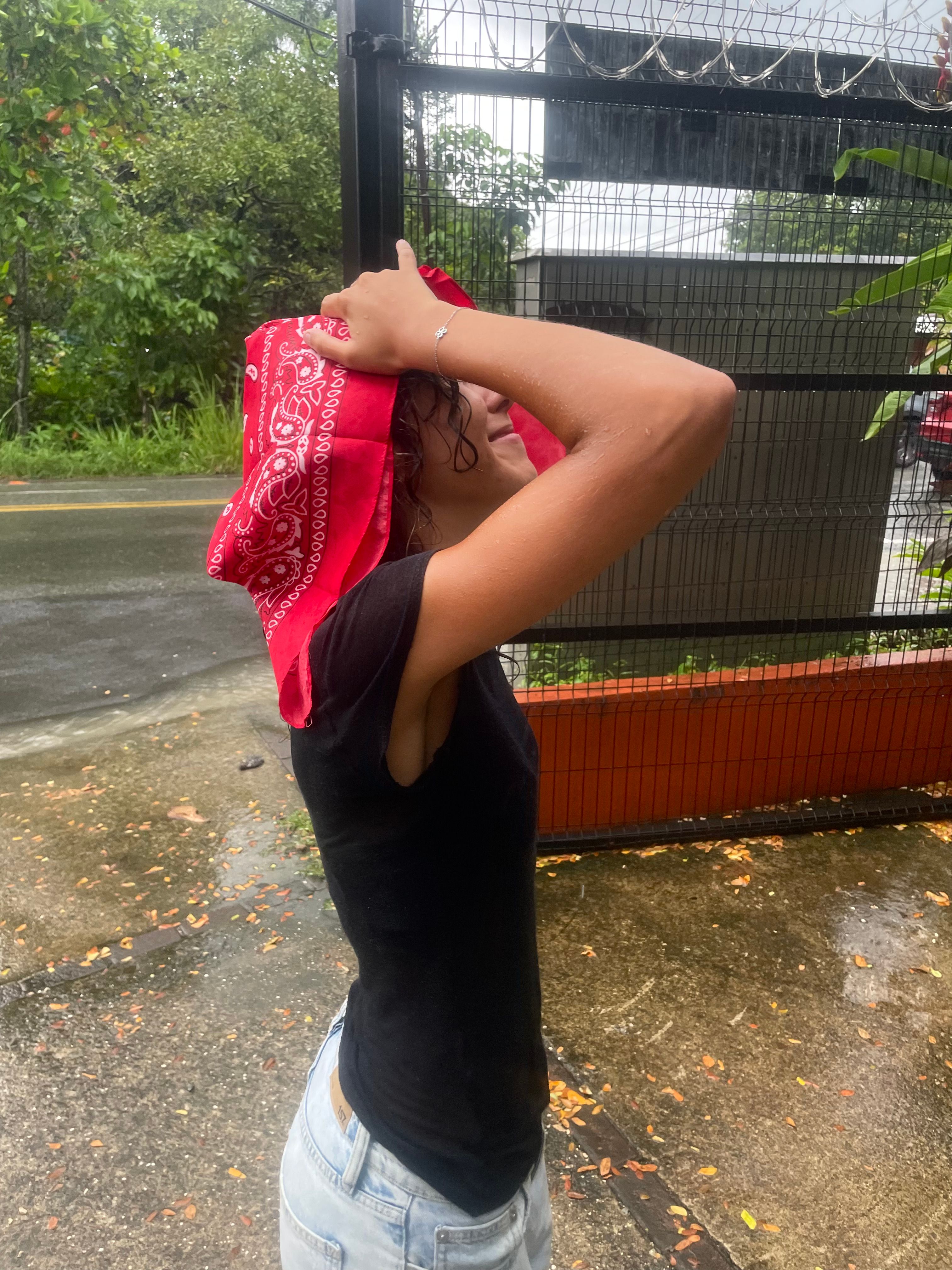 A person with a red bandana covering their head, standing in the rain.
