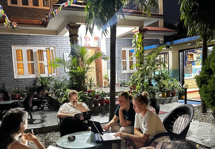 a group of people are sitting around a table with laptops
