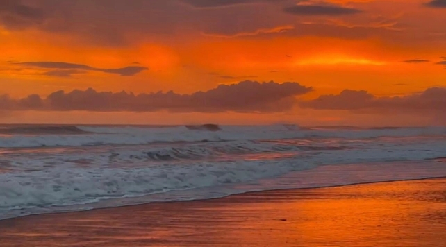 a sunset over the ocean with waves crashing on the beach