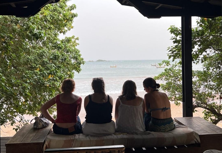 fire kvinner sitter på en benk og ser ut et vindu på havet.