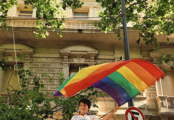 a boy holding a rainbow flag in front of a no parking sign