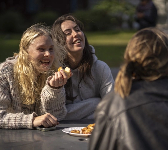 a group of young women are sitting at a table eating food and laughing .