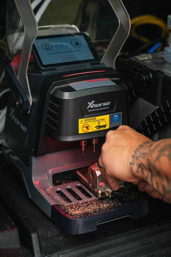 A technician cuts a car key on an Xhorse key machine inside the mobile locksmith van.