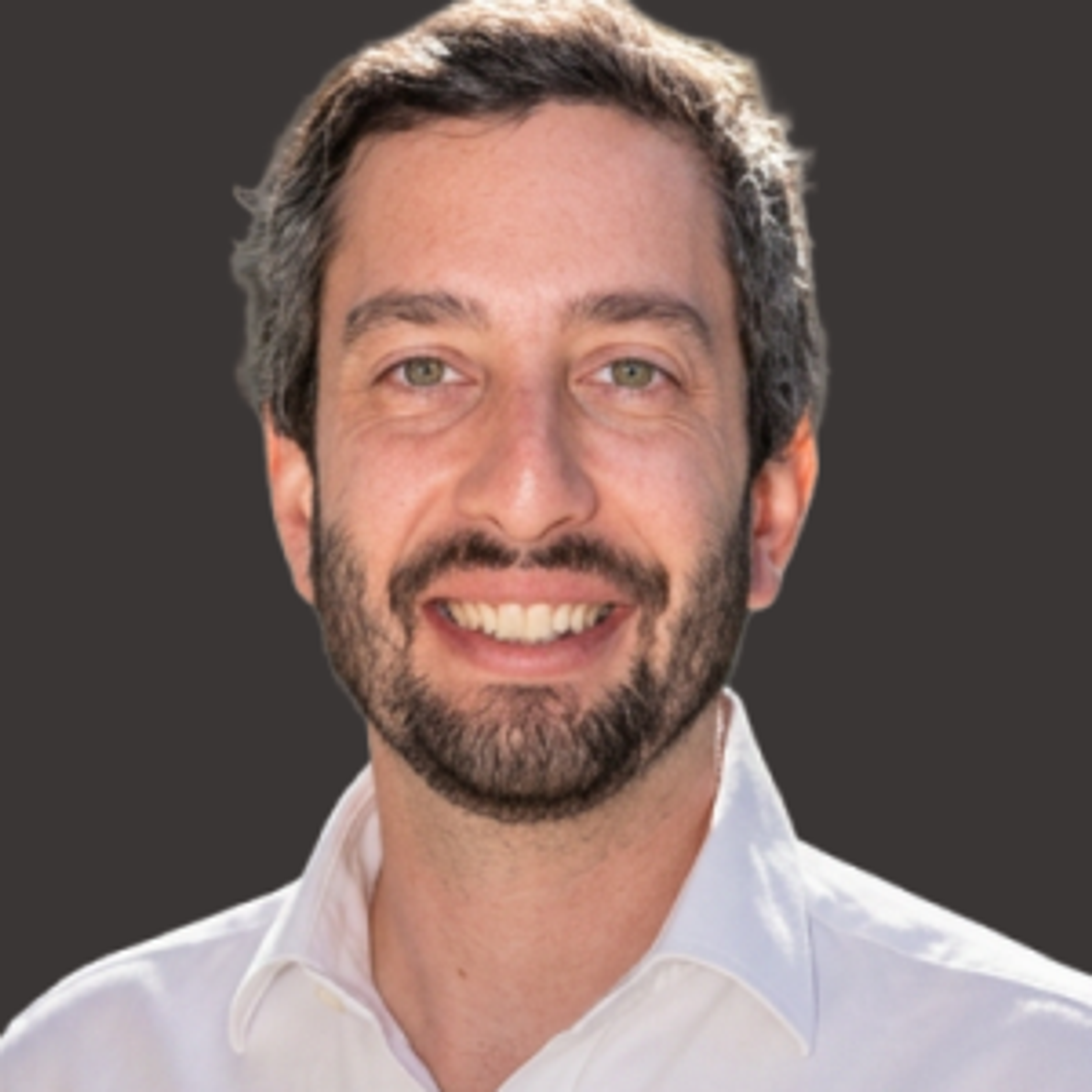 Smiling man with short, dark hair and a beard wearing a white collared shirt, posed against a plain dark background.