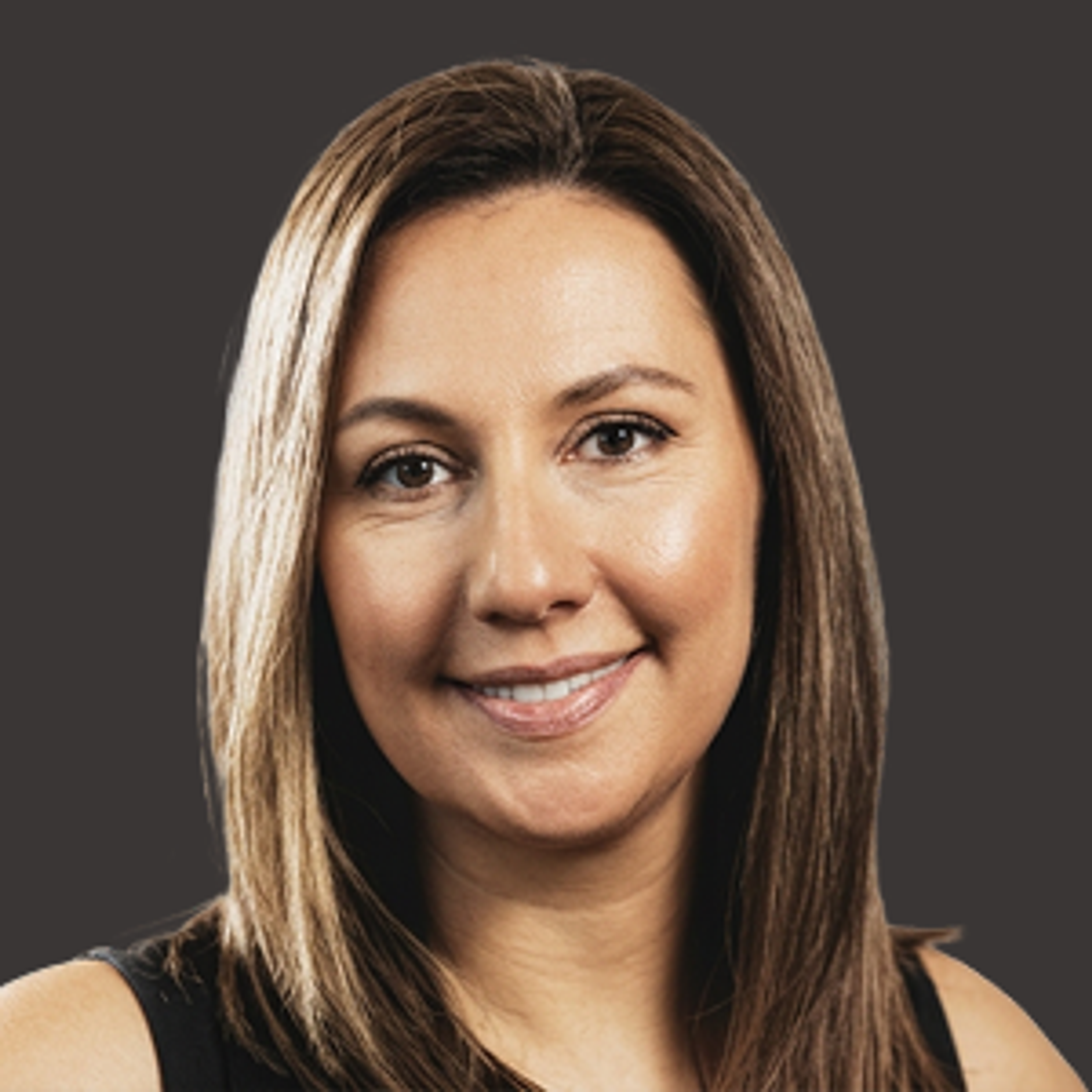 A woman with straight, shoulder-length brown hair smiles at the camera. She is wearing a sleeveless black top and is posed in front of a plain dark background.