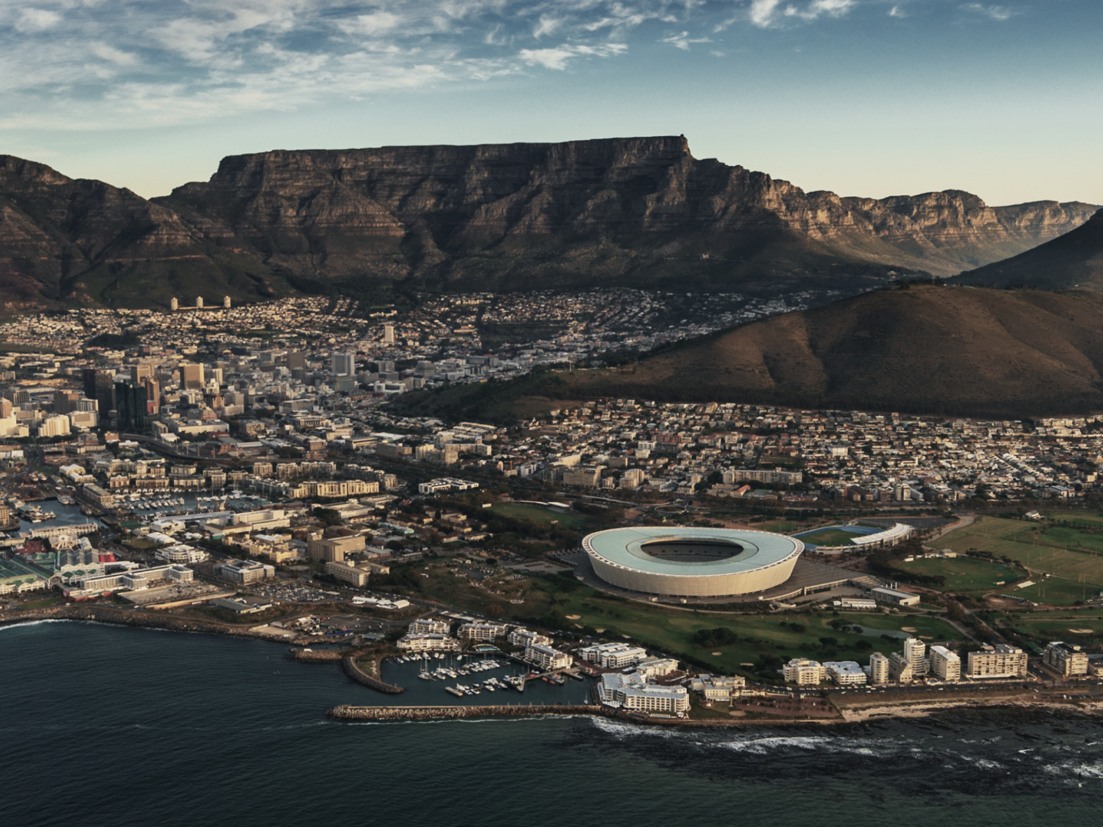 Aerial view of Cape Town, South Africa, featuring the Cape Town Stadium and Table Mountain in the background.