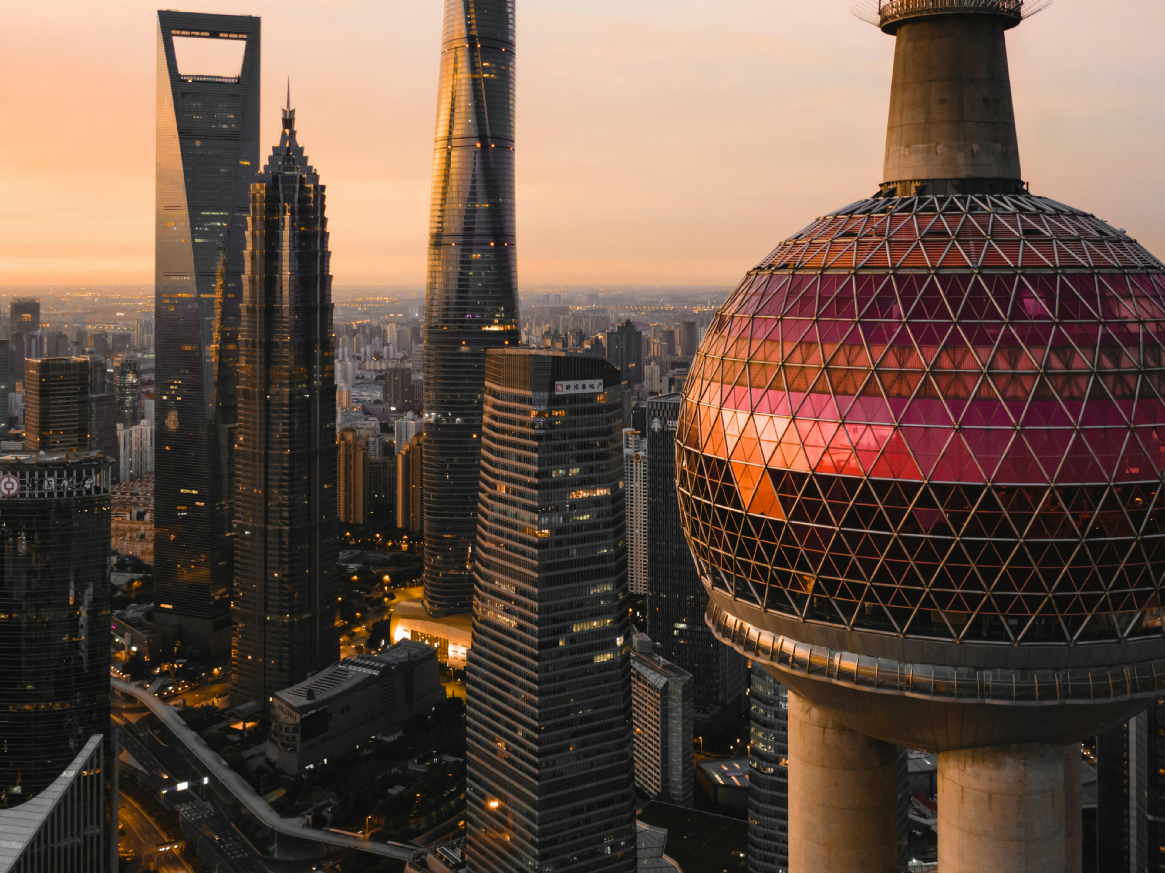 The Oriental Pearl Tower in the foreground, with the Shanghai skyline and its tall skyscrapers visible at sunset.
