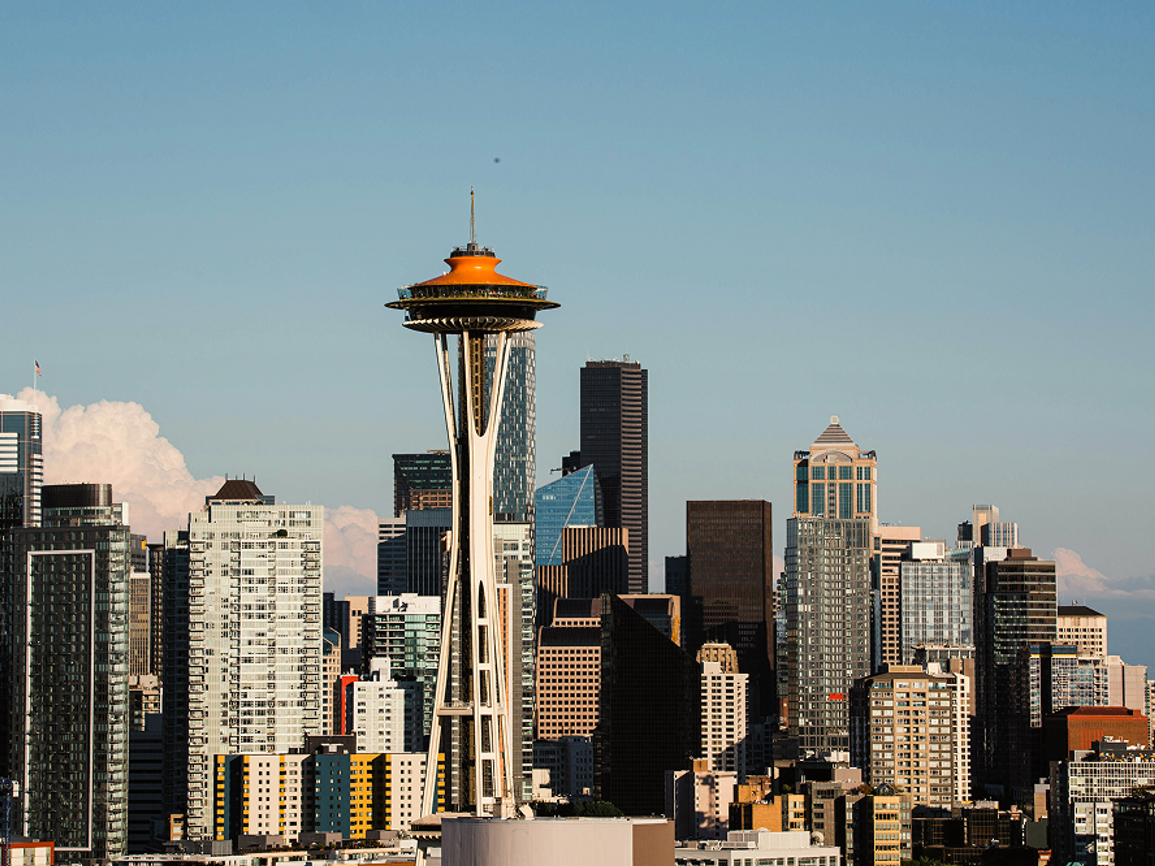 The Space Needle stands in front of the Seattle skyline with modern skyscrapers and a clear blue sky in the background.