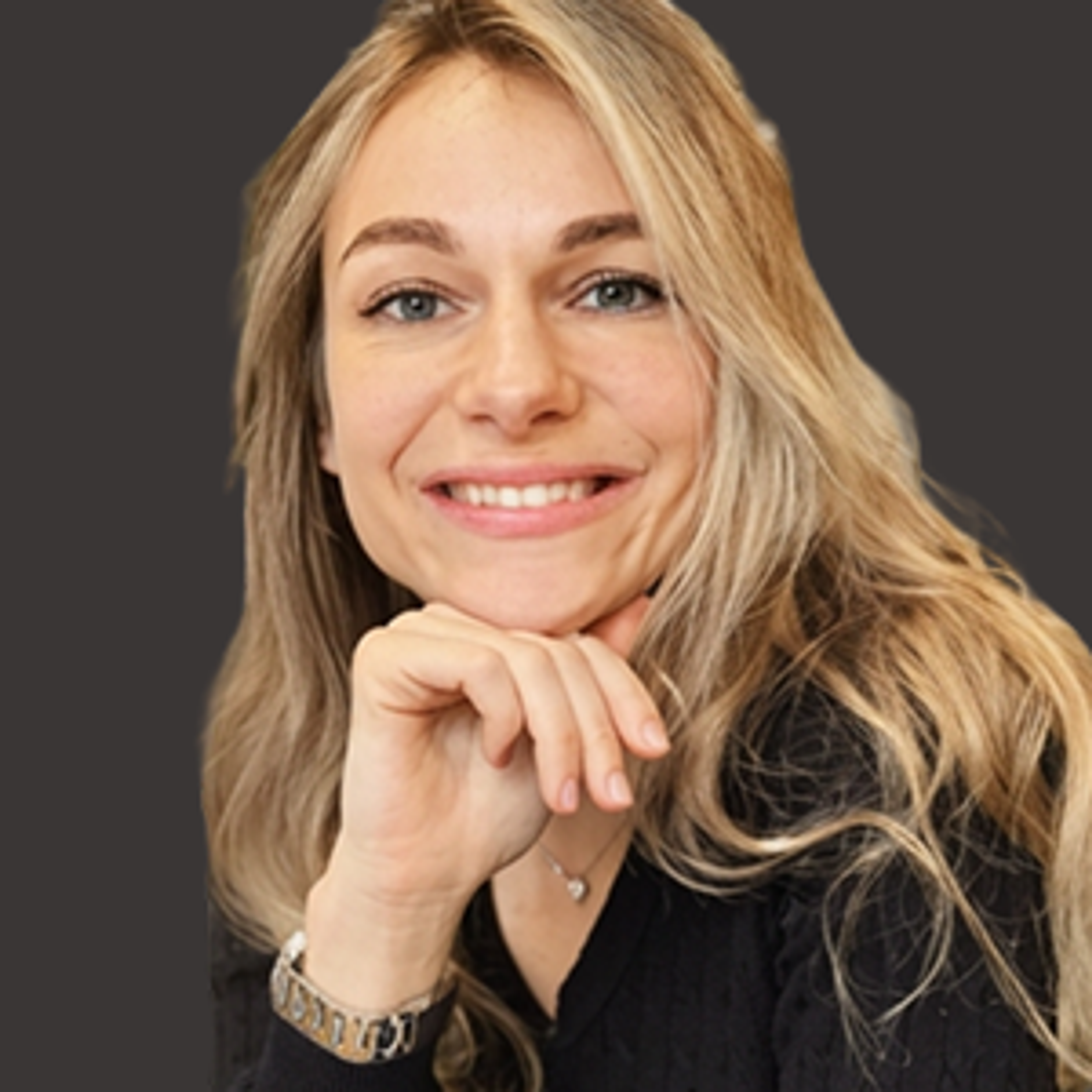 A woman with long blonde hair and a black top smiles at the camera, resting her chin on her hand, with a dark solid background.