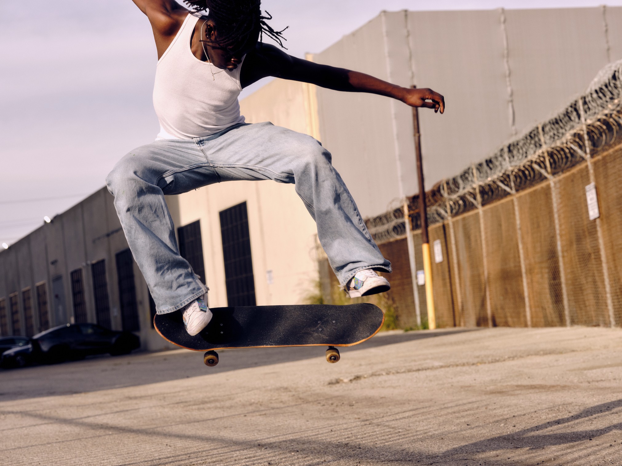 photo of an african-american man in baggy light blue unspun jeans performing a skateboard trick