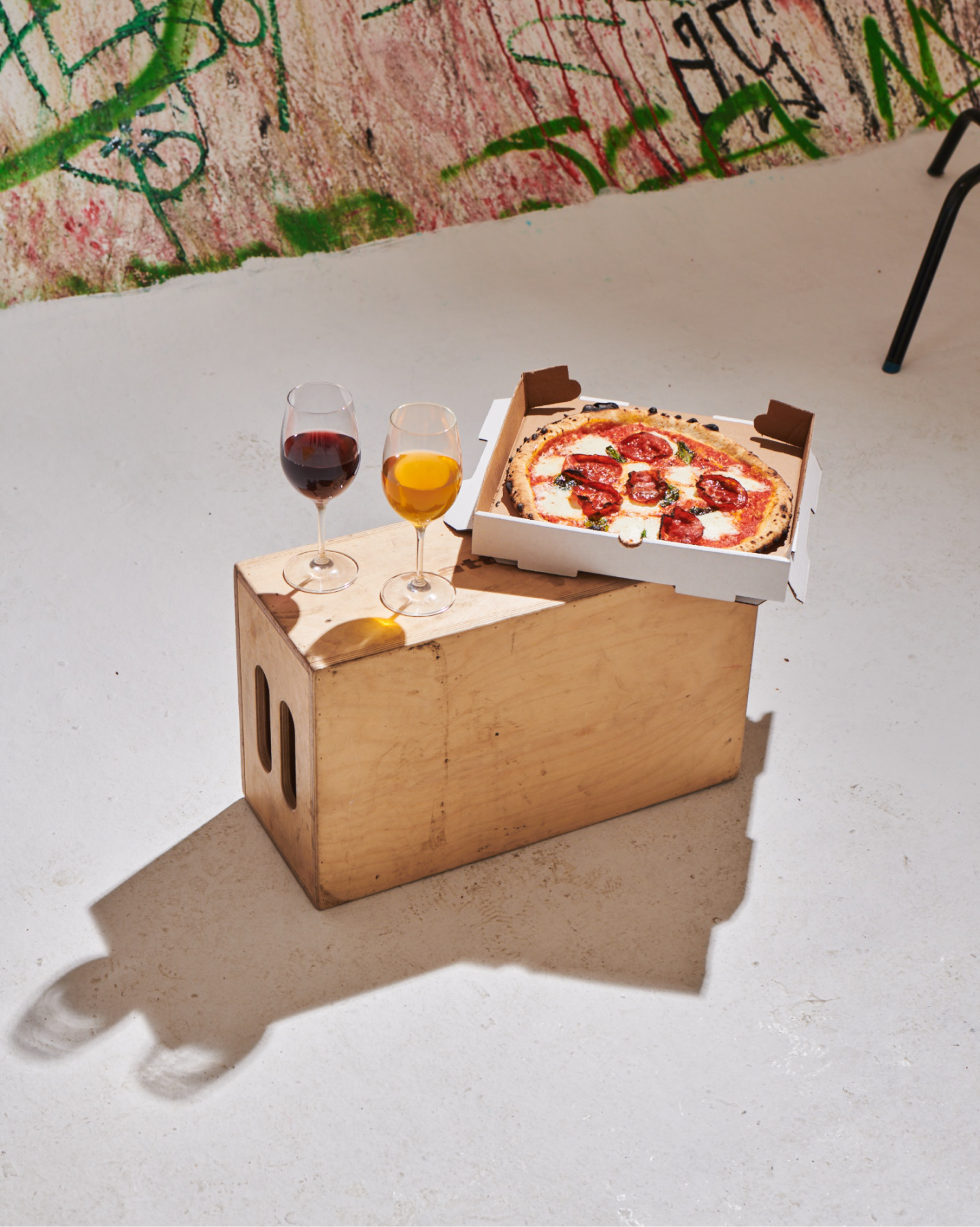 photograph of roberta's pizza and two wine glasses set on a wood box