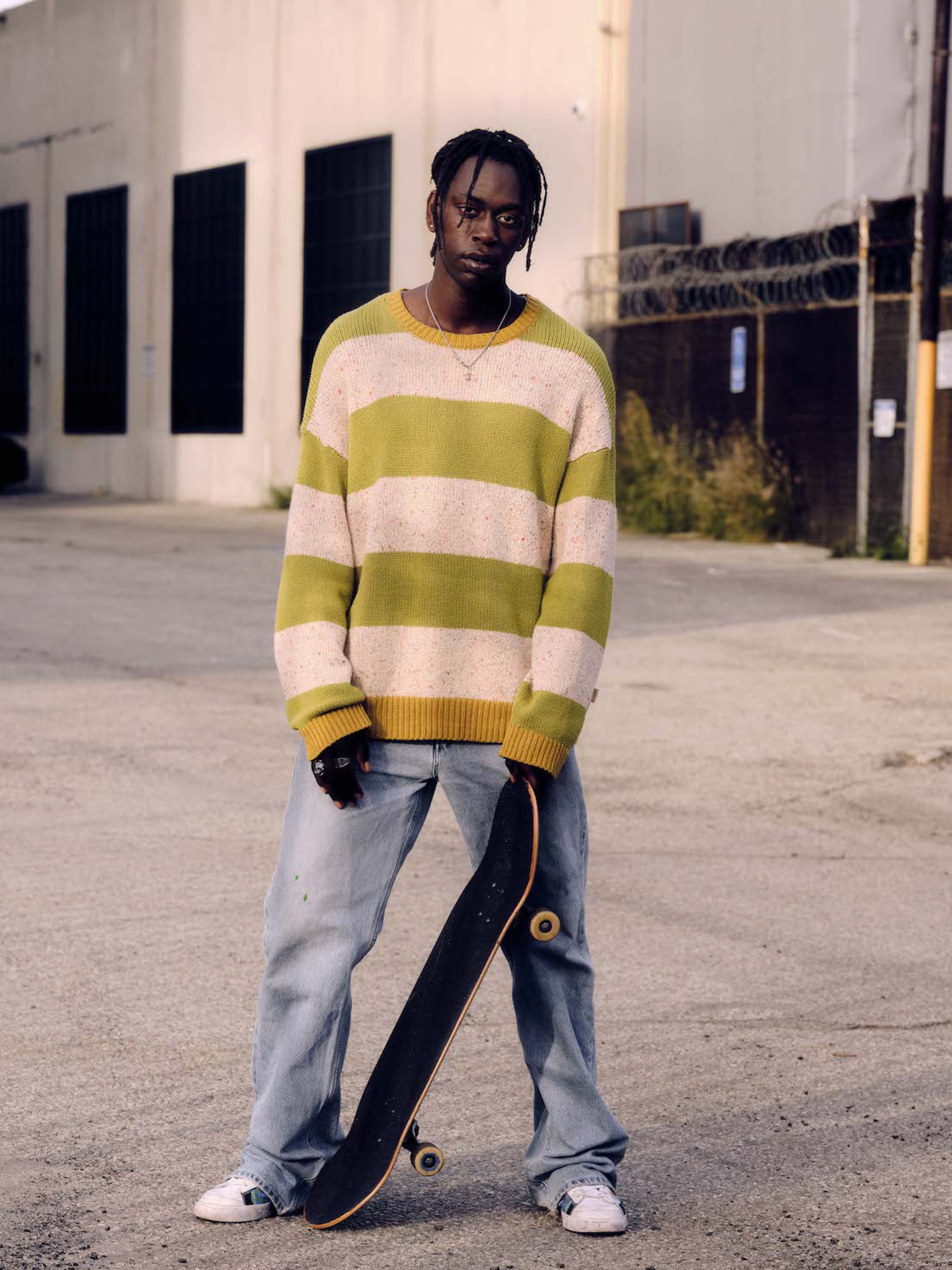 photo of an african-american man in striped sweater and light unspun jeans holding a skateboard
