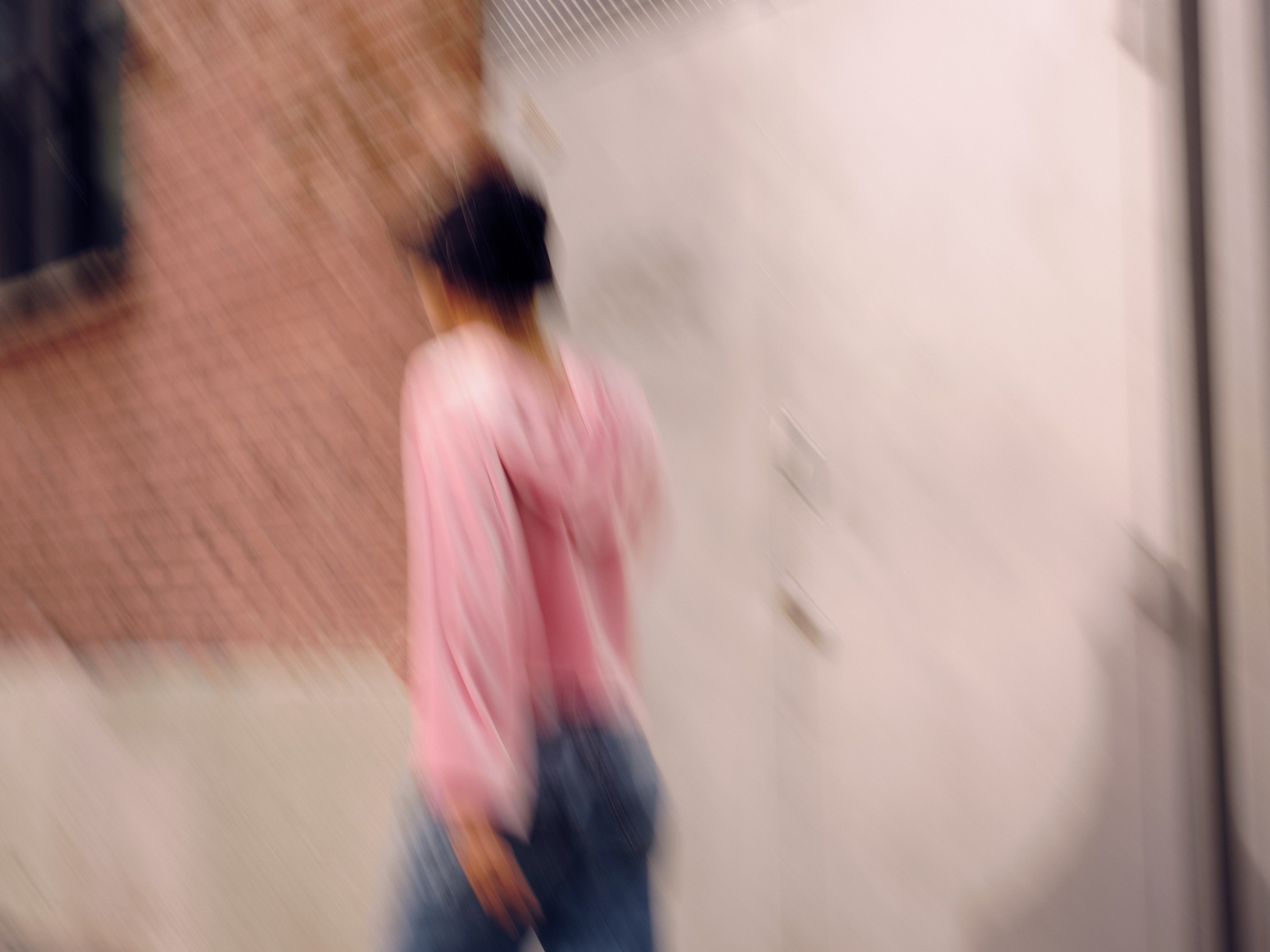 blurry photo of a man with bucket hat and pink jacket walking along a brick wall