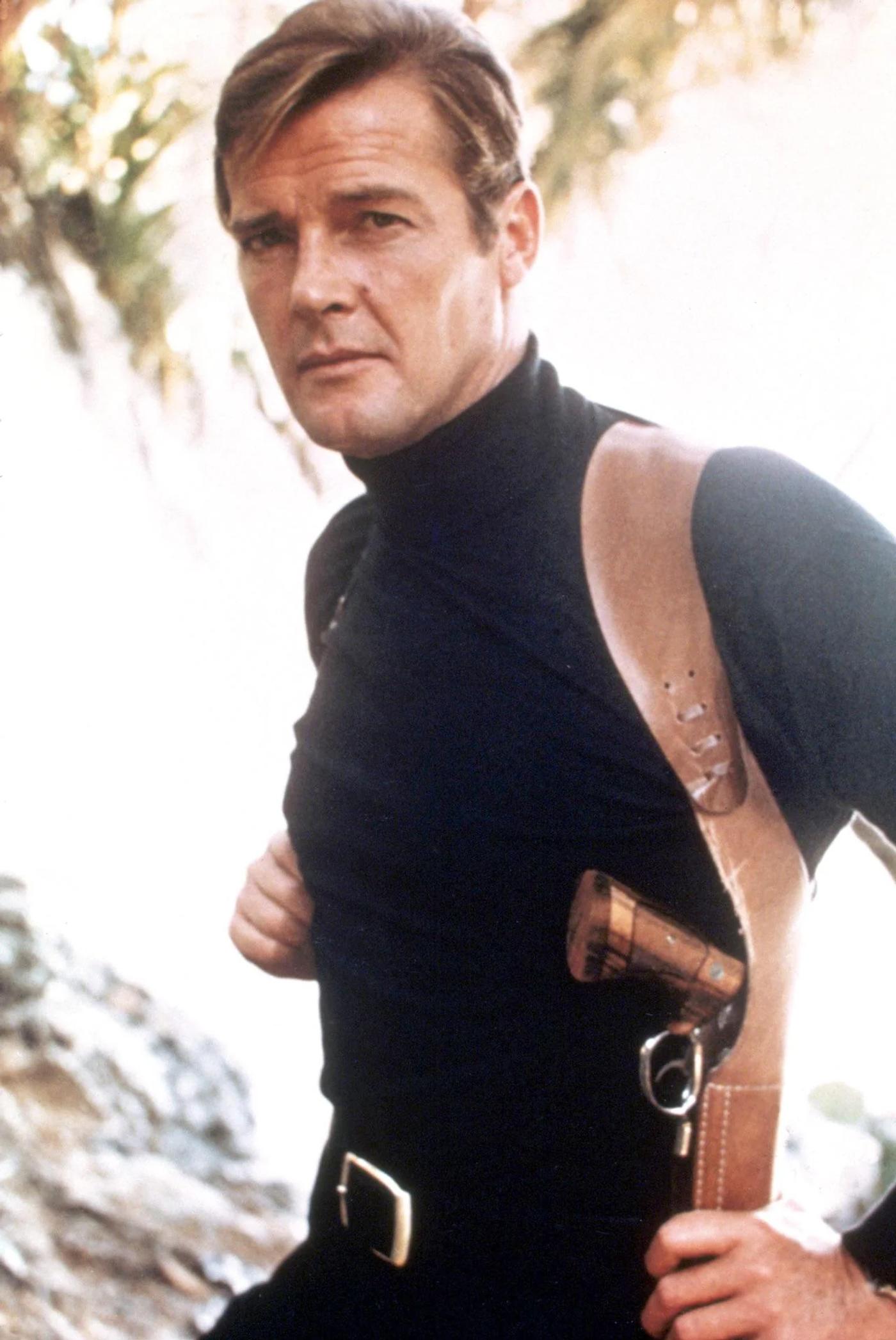 Roger Moore as James Bond wearing a black turtleneck, with a pistol in a shoulder holster.