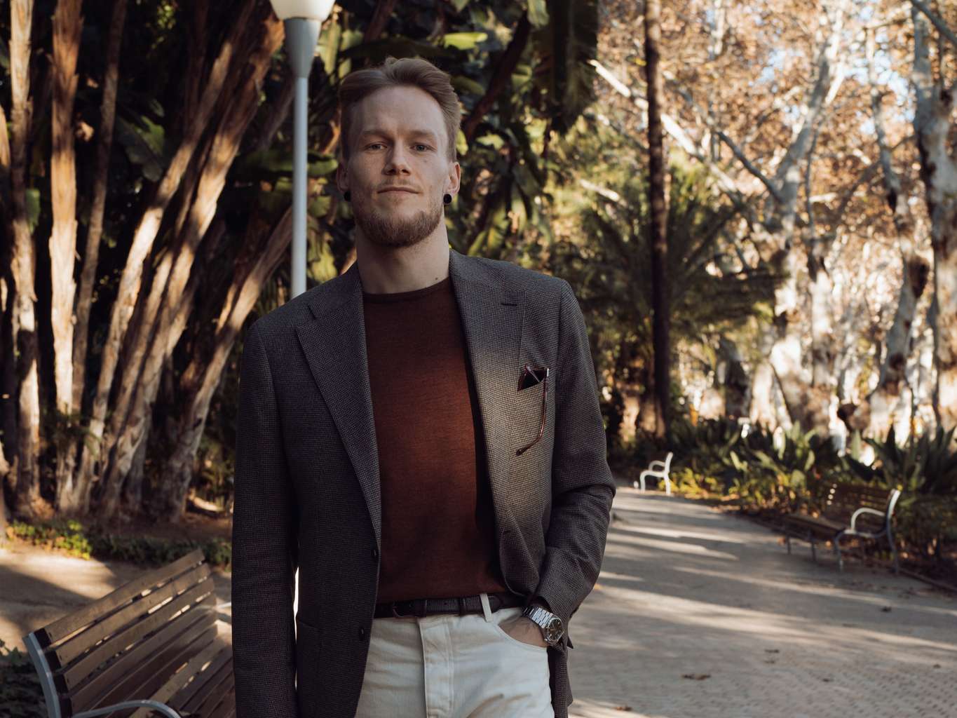 a man in a suit is standing in a park next to a bench .