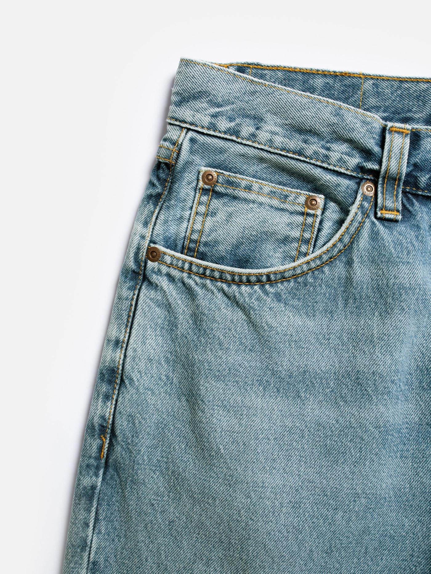 Close-up of light wash jeans showing a front pocket, coin pocket, waistband, yellow stitching, and metal rivets.