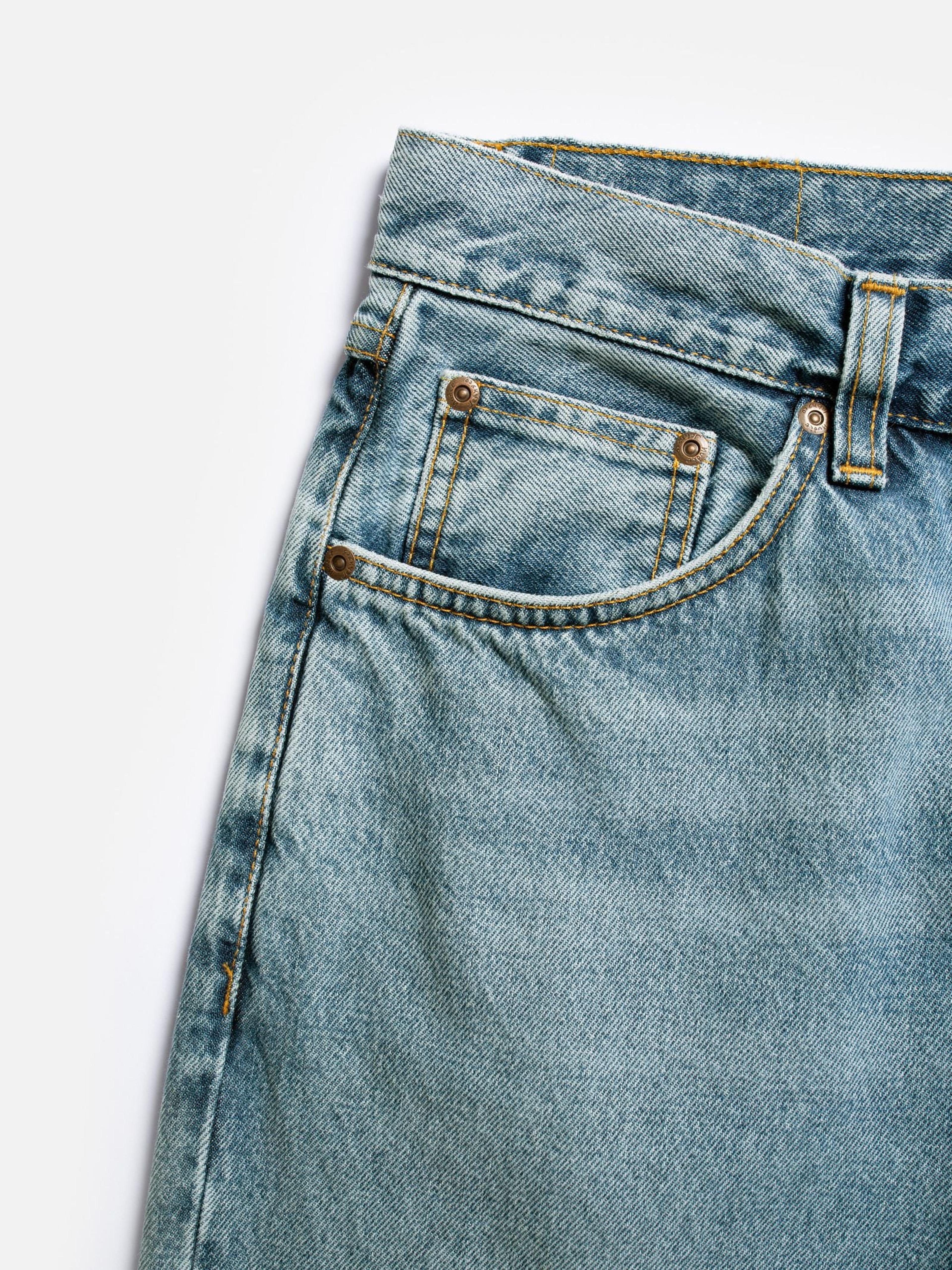 Close-up of light wash jeans showing a front pocket, coin pocket, waistband, yellow stitching, and metal rivets.