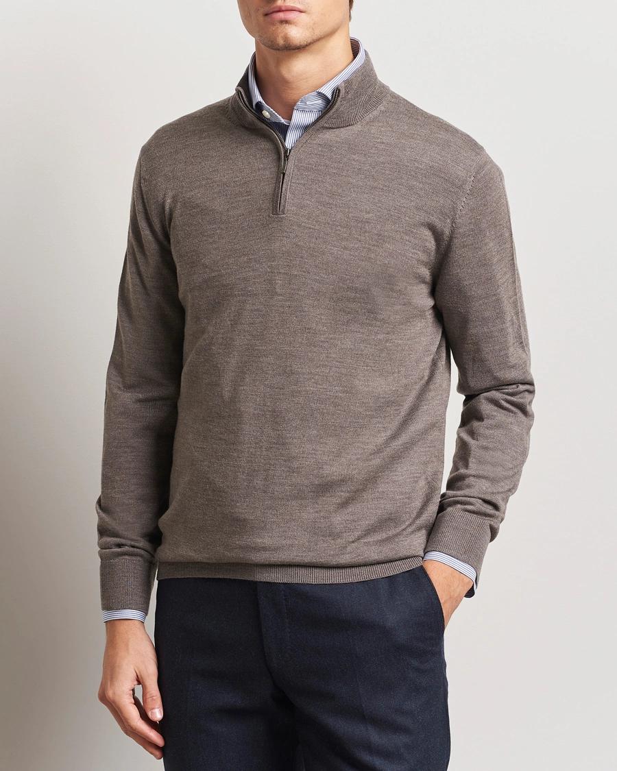 Man wearing a brown quarter-zip sweater over a blue striped shirt and dark trousers.