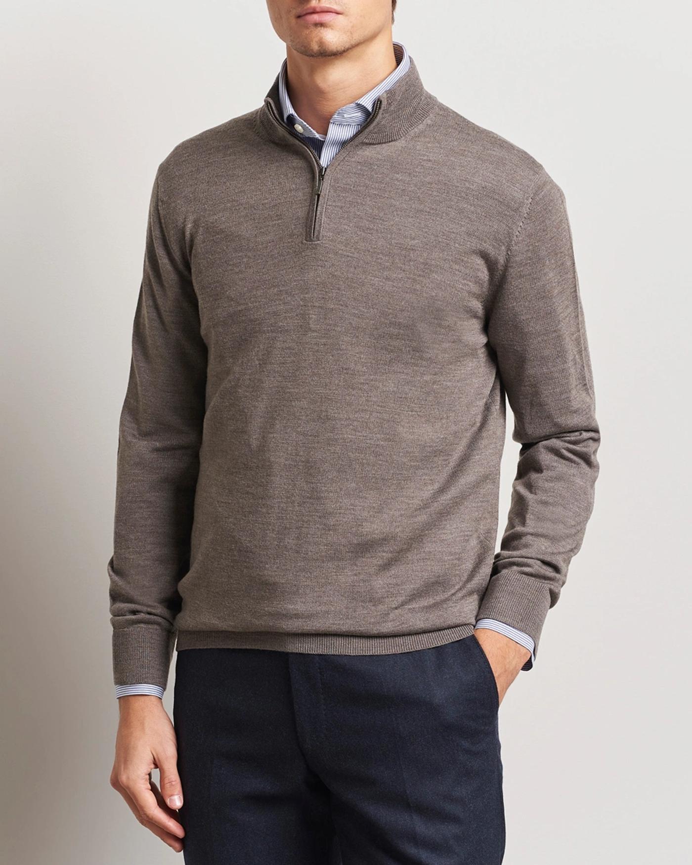 Man wearing a brown quarter-zip sweater over a blue striped shirt and dark trousers.