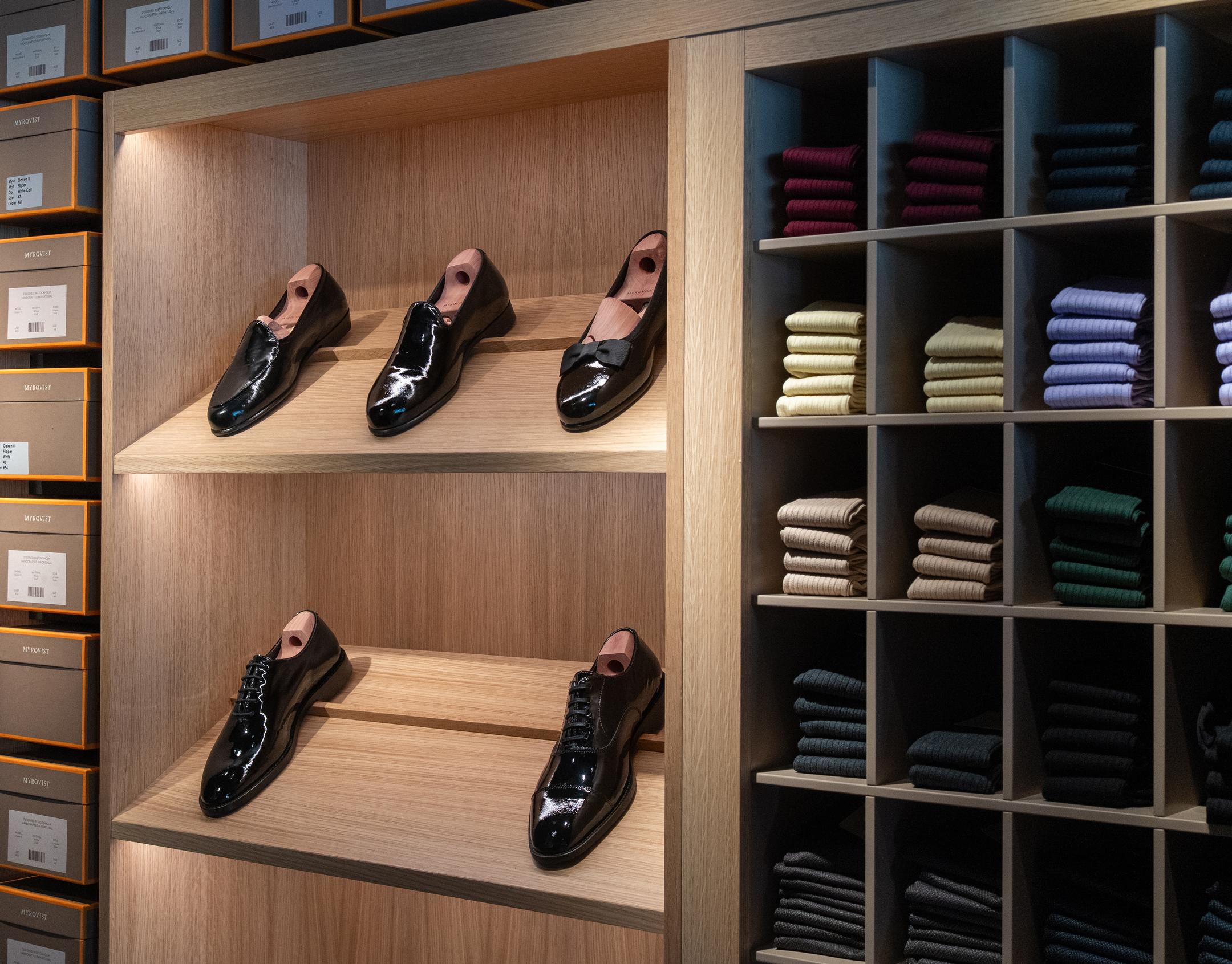 Patent leather shoes on wooden shelves next to colorful folded socks in cubbies.